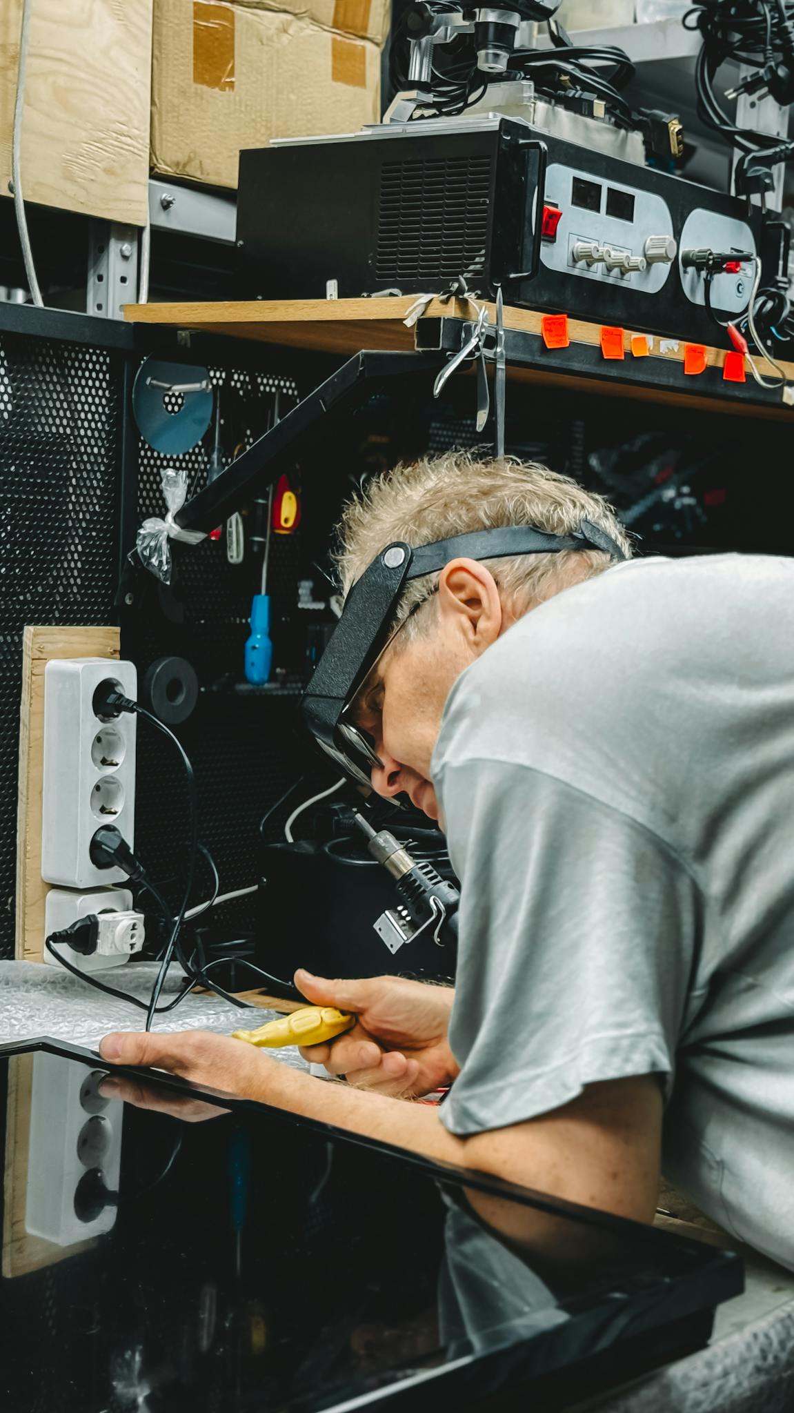 Professional technician working on electronic device repair in a cluttered workshop.